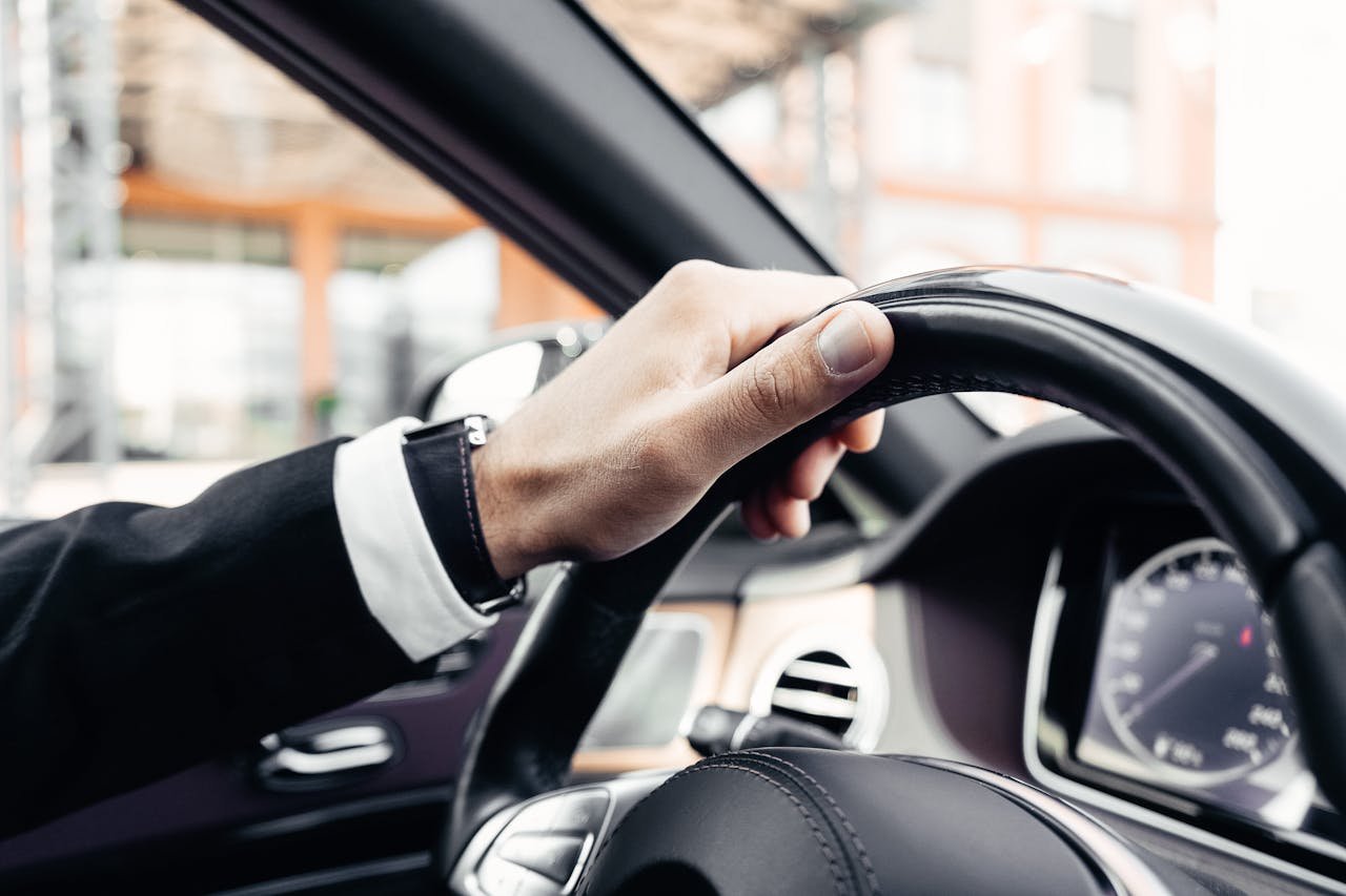 Services Elegant hand in a suit holding a modern car steering wheel, close-up shot inside a vehicle.