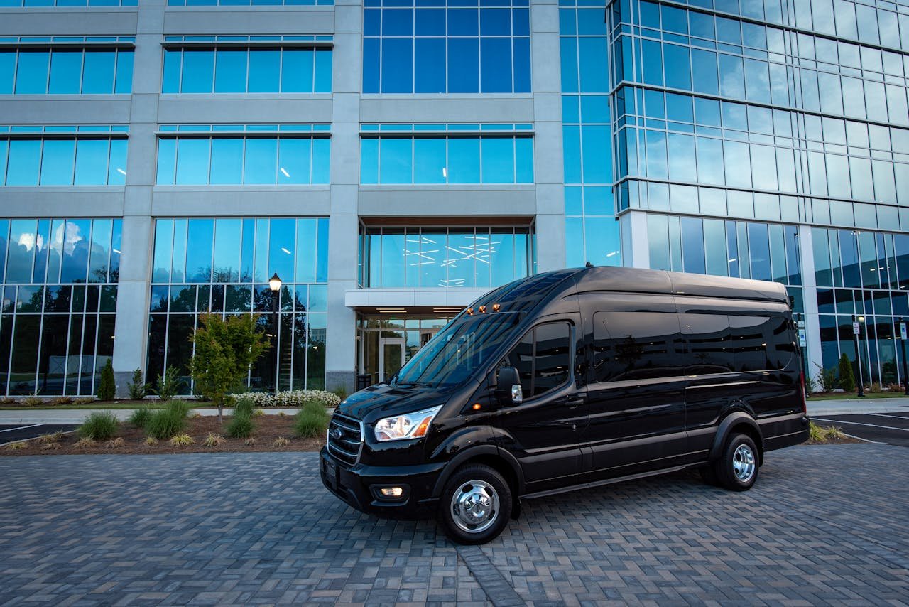Services Black luxury van parked in front of a modern office building under daylight.